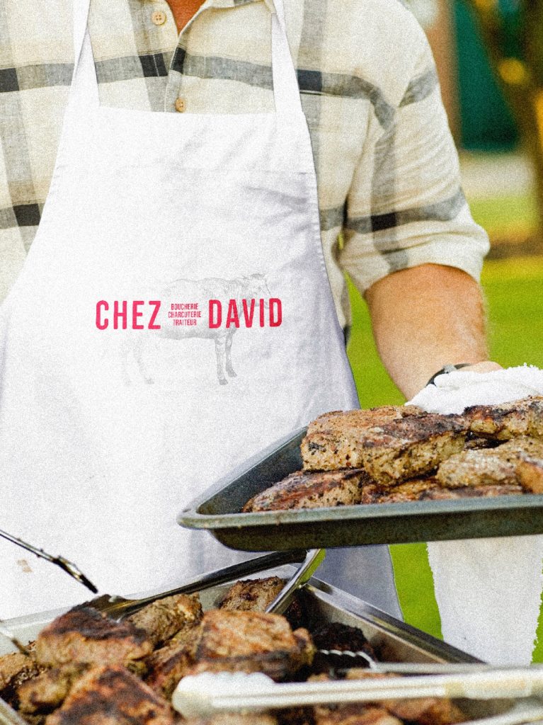 Tablier blanc Chez David porté devant des grillades